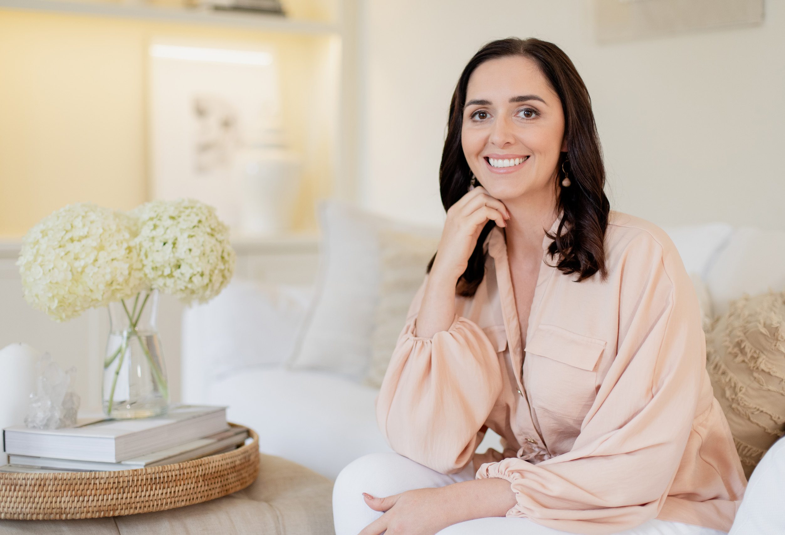 Natasha Leigh Bray Natasha Leigh Bray sitting on a sofa wearing a pink blouse and white jeans